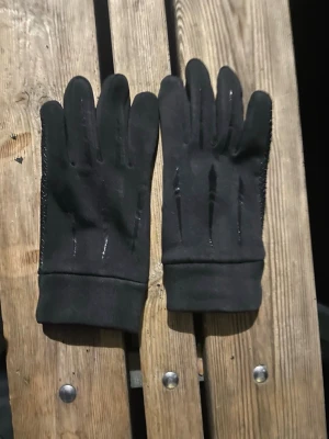 Svarta mockahandskar med grepp - Snygga svarta handskar i mocka med diskreta sömdetaljer på ovansidan och greppvänlig insida med små gummiprickar. Perfekta för kyliga dagar och ger ett stilrent intryck till din outfit.