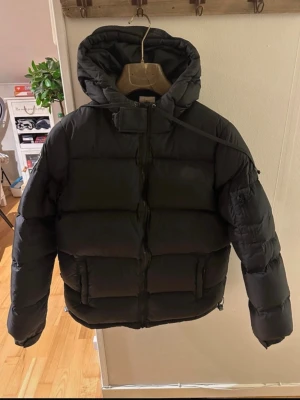 Svart dunjacka från Dbrand  med huva storlek xl  - Säljer en svart dunjacka från DB med huva och dragkedja framtill. Jackan har två stora fickor med dragkedja och en patch på ena ärmen. Puffig modell som håller värmen och har en sportig look. Perfekt för kalla dagar.