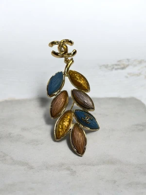 brosch med blad och logga - Unik brosch  i guldmetall med bladformade detaljer i blått, guld och brons. Broschen har den organiskt mönster. Perfekt accessoar för att lyfta din outfit med exklusiv känsla.