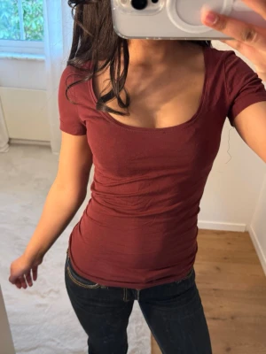 Vinröd tight topp - Säljer en så fin topp med rund, djup urringning och korta ärmar. Modellen är tight och sitter snyggt. Perfekt att styla med jeans eller kjol för en clean look!