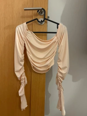 Ljusrosa omlottopp med rynkade ärmar - Trendig ljusrosa topp med omlottdesign och långa, rynkade ärmar. Toppen har en draperad framsida och är croppad i modellen. Perfekt för dig som gillar en unik och feminin stil.