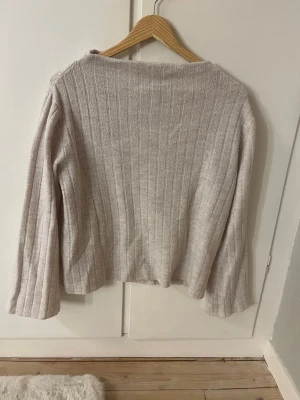 Stickad tröja  - Ljusbeige ribbstickad tröja från 157 med raka ärmar och avslappnad passform. Tröjan har diskreta lodräta ränder och är tillverkad i ett mjukt stickat material som känns skönt mot huden. Perfekt för lager på lager och enkel att matcha.