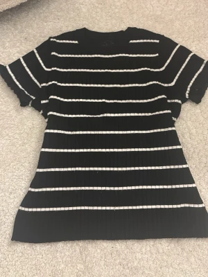 Svartvit randig ribbad topp - Snygg svart topp med vita horisontella ränder och ribbad struktur. Kortärmad modell med rund halsringning. Perfekt till jeans eller kjol för en avslappnad look.
