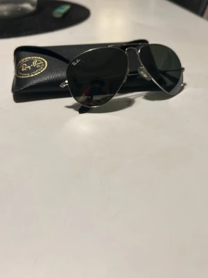 Ray-Ban Aviator solglasögon silver - Klassiska Ray-Ban Aviator solglasögon med silvrig metallbåge och mörka linser. Säljes med originalfodral i svart skinn. Perfekt accessoar för en cool och tidlös stil.