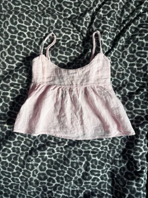 Ljusrosa linnetopp med tunna band - Supersöt ljusrosa linnetopp med tunna axelband och lätt utställd passform. Toppen är gjord i ett luftigt linnematerial och har en mjuk, flowy siluett som passar perfekt till varma dagar. Aldrig använd. Tvättad 1 gång. Nypris 249kr