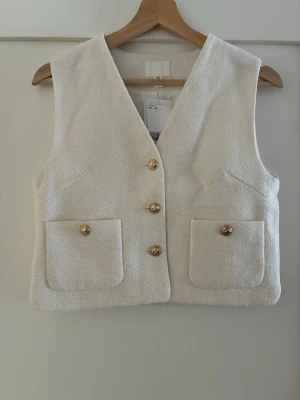 V-ringad boucléväst - En figurnära väst i bouclé med v-ringning och knäppning fram. Utanpåfickor med knapp fram.  Helt ny. Köpt förra hösten. Orig. pris 349kr  Från rökfritt hem men vi har hundar