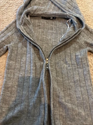 Grå ribbad hoodie med dragkedja - Säljer en grå ribbad hoodie från 157 med dragkedja framtill och huva med snören. Hoodien är tillverkad i mjukt stickat material och har en avslappnad passform. Perfekt för dig som gillar en enkel och stilren look.