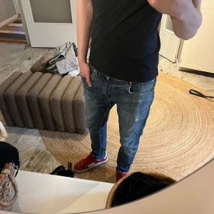 Blå raka jeans tiger of sweden - Säljer ett par klassiska blå jeans med rak passform och snygga slitningar. Jeansen har fem fickor och en brun läderpatch bak i midjan. Perfekta till vardagslooken och passar till det mesta. Materialet är denim i bomull.