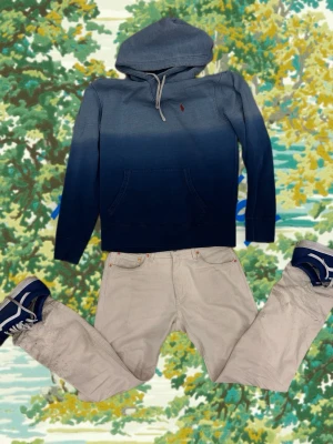 Blå hoodie från Polo Ralph Lauren - Snygg hoodie från Polo Ralph Lauren i en cool blå ombre-färg. Klassisk huva med dragsko och stor magficka framtill. Liten röd logga broderad på bröstet. Perfekt för en avslappnad och trendig look.