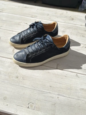 Max martini - Stilrena svarta sneakers i läder med vita sulor och mörkblå skosnören. Insidan är fodrad i beige och skon har en klassisk låg profil. Perfekta för dig som gillar en clean och tidlös look.