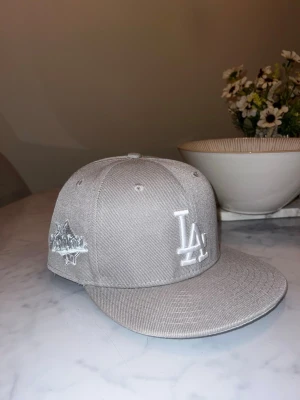 Grå LA Dodgers keps från New Era 7 1/2 - Säljer en stilren grå keps från New Era med LA Dodgers-logga broderad i vitt framtill och en specialpatch på sidan. Perfekt för dig som vill ha en clean och sportig look.