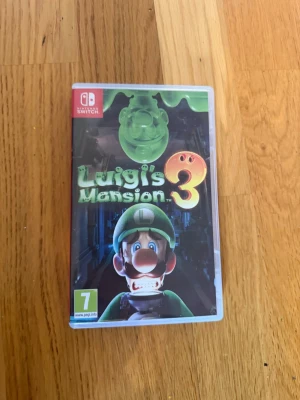 Luigi's Mansion 3 till Nintendo Switch - Luigi's Mansion 3 är ett äventyrsspel till Nintendo Switch där du spelar som Luigi och utforskar ett spöklikt hotell fullt av utmaningar och pussel. Omslaget är färgstarkt med gröna och svarta toner och spelet levereras i ett klassiskt plastfodral.
