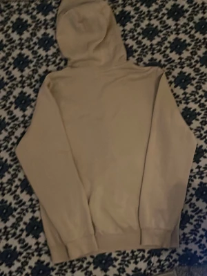 Beige hoodie från McKenzie - Säljer en beige hoodie från McKenzie med klassisk huva och magficka. Tröjan har ribbade muddar vid ärmslut och nederkant samt en liten vit McKenzie-logga på bröstet.