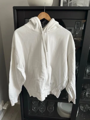 Vit oversized hoodie med huva - Säljer en vit oversized hoodie med huva och dragsnören. Hoodien har en stor magficka framtill och ribbade muddar vid ärmslut och nederkant. Perfekt för en avslappnad och stilren look. Materialet känns mjukt och skönt mot huden.