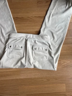 Vita mjukisbyxor Juicy Couture XS - Säljer ett par vita mjukisbyxor från Juicy Couture i storlek XS. Byxorna har två bakfickor med lock och knappdetaljer samt bred resår i midjan. Tillverkade i mjukt och skönt material som passar perfekt för en avslappnad stil. Betalning via vanlig swish!!