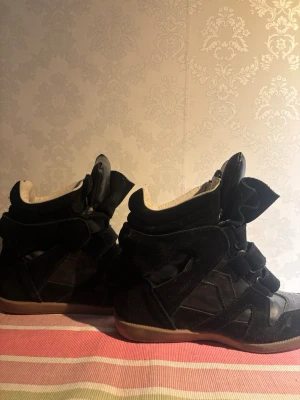 isabell marants skor - Snygga svarta sneakers med högt skaft och flera kardborreband.  Vet ej om du 100 procent äkta för de är köpta på vinted. Skorna har en mix av mocka och läderdetaljer samt en beige innersida och brun sula. Perfekta för dig som gillar streetstyle och vill sticka ut lite extra.