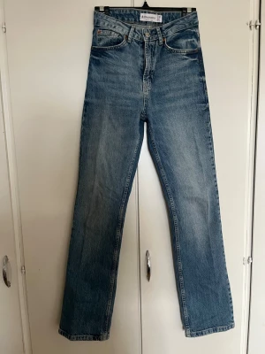 D98 Blå raka jeans från Stradivarius - Säljer ett par klassiska blå jeans från Stradivarius i rak modell med hög midja. Jeansen har fem fickor, knappgylf och är tillverkade i slitstark denim. Perfekta till en avslappnad look och passar till det mesta i garderoben.