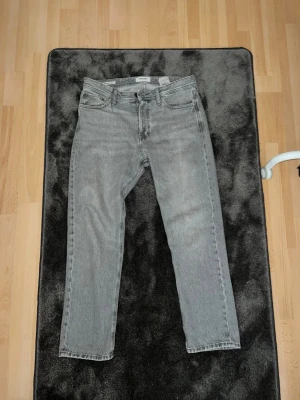 Grå raka jeans från Jack & Jones  - Säljer ett par klassiska grå Levi's jeans med rak passform och fem fickor. Jeansen har en tidlös look med normal midja och dragkedja. Tillverkade i slitstark denim som passar perfekt till en avslappnad stil. W 30 L 30 