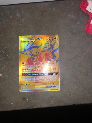 Pokémonkort Reshiram & Charizard GX - Säljer ett Pokémonkort med Reshiram & Charizard GX Tag Team. Kortet är holografiskt med guldfärgad bakgrund och detaljer i rött och blått. Det har attacker som Outrage, Flare Strike och Double Blaze GX. Perfekt för samlare eller Pokémonfans.