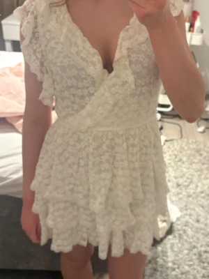 Vit spetsklänning med volanger - Supersöt vit kortklänning med omlott och v-ringning. Klänningen har spetsdetaljer, volanger i flera lager och korta ärmar. Perfekt för sommaren och skolavslutningen🫶🏻använd en gång 