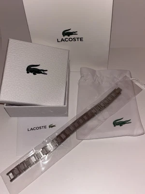 Lacoste Metropole Armband  - Lacoste Metropole Armband i rostfritt stål, helt nytt aldrig använt. Allt som finns på annonsen följer med dessutom är det snabb leverans och en väl packad paket. i storlek M (ungefär 18,5 cm) men det går att spänna för att kunna göra den mindre. Perfekt som present 