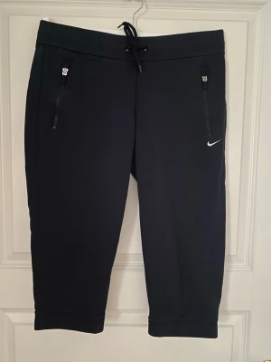 Svarta träningsshorts från Nike - Svarta träningsshorts från Nike med snörning i midjan och dragkedjeförsedda fickor framtill. Klassisk Nike-logga broderad i vitt på ena benet. Sköna och funktionella shorts i mjukt material, perfekta för sport och aktivitet. Kolla gärna mina andra annonser❗️