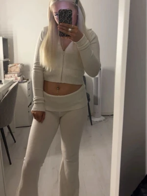 ”Lounge wear” set från Nelly  - Säljer ett set med vit ribbstickad cropped kofta med dragkedja framtill och långa ärmar. Koftan har en tight passform och ribbad mudd vid ärmslut och nederkant. +byxorna💕, använt fåtal gånger