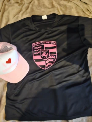 Svart papi Santana t-shirt med rosa tryck - Cool svart t-shirt från Santana med ett stort rosa emblem på bröstet där det står Falsterbo. T-shirten har rund halsringning och är kortärmad. Materialet känns sportigt och lätt, perfekt för en avslappnad stil.