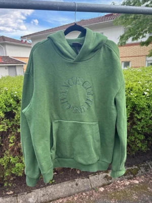 Grön hoodie - Snygg grön hoodie från Club Influence med broderad logga i cirkel på bröstet. Hoodien har en stor känguruficka framtill, huva och ribbade muddar vid ärmslut och nederkant. Perfekt för en chill och avslappnad stil. Den är lite nopprig då den är använd men annars jättesnygg och fin färg