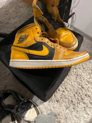 Air Jordan 1 Retro High OG Gul/Svart - Gula och svarta Air Jordan 1 Retro High OG med klassisk vinge-logga på sidan och svart swoosh. Skorna har högt skaft, perforerad tåbox och är tillverkade i läder med textildetaljer på plösen. Ikonisk siluett som sticker ut med sin färgkombination. Snörerna kommer med men ska tvätta upp de innan jag skickar de.