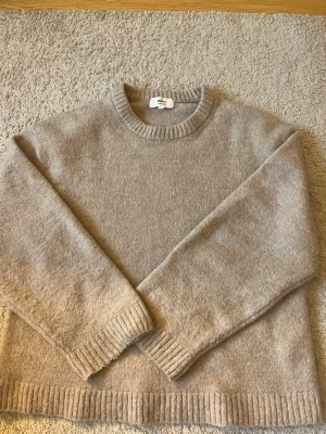 Beige stickad tröja från Gina Tricot - Mysig beige stickad tröja från Gina Tricot i ullblandning. Tröjan har rund halsringning, ribbstickade muddar vid ärmslut och nederkant samt en avslappnad passform. Perfekt för lager-på-lager och chill dagar.