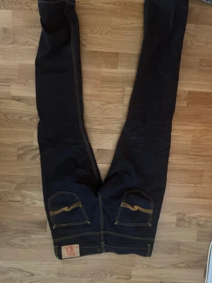 Jeans  - Snygga svarta jeans från Nudie Jeans med klassisk femficksdesign och kontrasterande orange sömmar. Jeansen har raka ben och är tillverkade i ett slitstarkt denimtyg. Perfekta för en stilren och avslappnad look. ( aldrig använda)