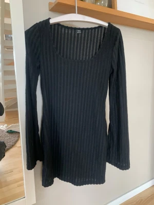 Svart ribbad långärmad klänning - En svart, ribbad kortklänning med lång ärm och rundad urringning. Klänningen har en kroppsnära passform och är tillverkad i ett stretchigt material som känns bekvämt mot huden. Perfekt för dig som gillar en enkel men stilren look.