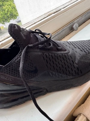 Nike Air Max 270 helsvart sneaker - Nike Air Max 270 sneakers i helsvart färg med mesh-överdel och synlig Air Max-sula. Skon har en sportig siluett, snörning och diskret Nike-logga på sidan. Perfekt för dig som gillar streetwear och vill ha en clean look.