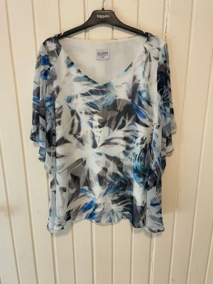 Blommig blus från Allison - Snygg blus från Allison med blommigt mönster i blått, vitt och grått. Blusen har v-ringning och luftiga, vida ärmar. Tillverkad i ett tunt och lätt material som ger en flowy känsla. Perfekt för dig som gillar en avslappnad men trendig stil.