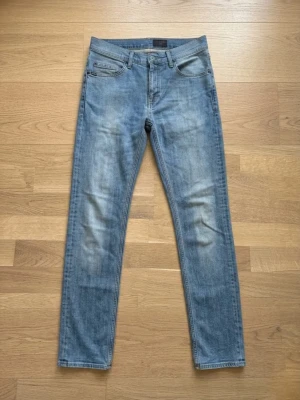 Tiger of Sweden – Pistolero Slim-Fit Jeans - Klassiska slim-fit jeans från Tiger of Sweden i modellen "Pistolero". De har en avsmalnande passform (tapered leg) och är gjorda i "comfort stretch" (99% bomull, 1% elastan), vilket gör dem både snygga och väldigt bekväma att bära. Sitter normalt i midjan (mid-waist). Stilrena detaljer med logopatch i Jacron på baksidan och diskreta sömmar på bakfickorna. Pris kan diskuteras vid snabb affär