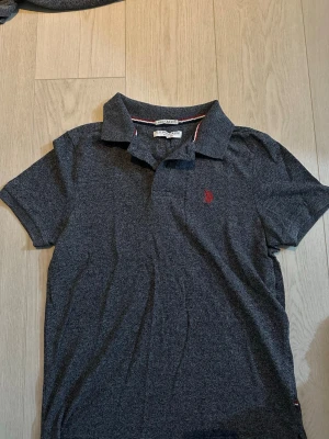 Mörkblå pikétröja från Ralph Lauren - Klassisk mörkblå pikétröja från Ralph Lauren med korta ärmar och krage. Tröjan har en röd broderad logga på bröstet och är tillverkad i mjuk bomull. Perfekt för en stilren och avslappnad look.