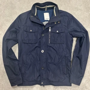 J.Lindeberg Fieldjacket  - Säljer denna mörkblå Fieldjacket från J.Lindeberg! Jackan är i väldigt bra skick. Inga defekter förutom att jag spillt lite cola på insidan, detta syns ej vid använding då det är på insidan av jackan. Storlek L. Modellen på bilden är 182cm ish. Skriv vid funderingar!