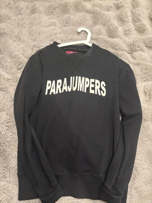 Svart fleece-tröja från Parajumpers - Svart långärmad fleece-tröja från Parajumpers med vit logotyp på bröstet. Tröjan har rund halsringning och ribbade muddar vid ärmslut och nederkant. Perfekt för dig som gillar stilrena och bekväma plagg.