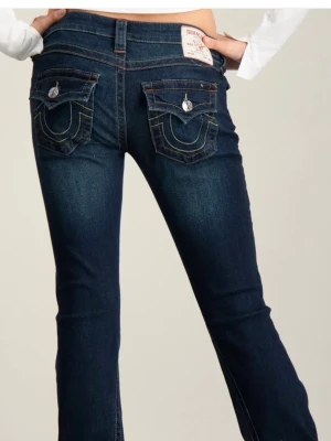 Mörkblå bootcut jeans True Religion - Snygga mörkblå bootcut jeans från True Religion med ikoniska bakfickor med lock och kontrastsömmar. Jeansen har låg midja, klassisk femficksdesign och är tillverkade i stretchig denim för en bekväm passform. Jag har sytt upp jeansen där nere men det är inget man ser, de passar någon som är ca 163 cm