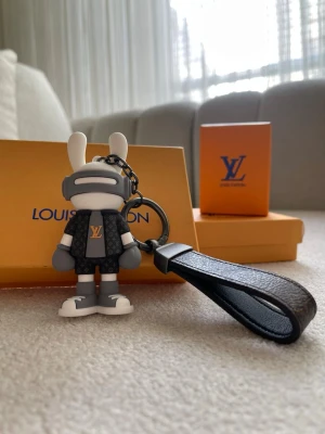  Vuitton kanin nyckelring - Cool nyckelring från  Vuitton i form av en kaninfigur med grå och vita detaljer samt LV-logga på tröjan. Nyckelringen har en mörkbrun läderrem med klassiskt monogrammönster. Perfekt accessoar till väskan eller nycklarna.