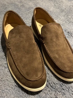 Bruna mockaloafers med vit sula - Snygga bruna loafers i mocka från HIVB med stilren design och vit gummisula. Skorna har en klassisk slip-on-modell och är perfekta för en chill och avslappnad look. Mjukt innerfoder för extra komfort.