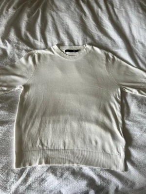 Vit kortärmad topp i bomull - En stilren vit topp med korta ärmar och rund halsringning. Tillverkad i mjuk bomull med ribbade detaljer vid ärmslut, hals och nederkant. Perfekt för en clean och enkel look.