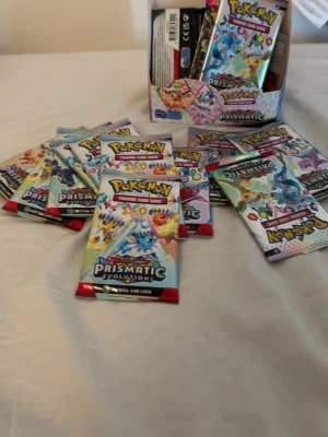 Pokémon Prismatic Evolutions boosterpack - Flera oöppnade Pokémon Prismatic Evolutions boosterpack med färgglada förpackningar. Perfekt för samlare eller dig som vill bygga din kortlek. Varje paket innehåller slumpmässiga samlarkort från Pokémon Trading Card Game.
