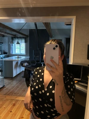 Svart prickig omlottopp - Snygg svart omlottopp med vita prickar och v-ringning. Den är i storlek L men den sitter mer som en M/S tycker jag. Toppen har korta ärmar och croppad passform som ger en trendig look. Perfekt att matcha med höga byxor eller kjol för en cool stil.