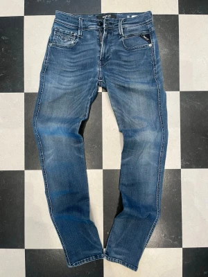 Replay Anbass W30 - Snygga blå slim fit jeans från Spray med klassisk femficksdesign och ljusa slitningar framtill och baktill. Jeansen har normal midja, smal passform och detaljerade bakfickor med broderi. Perfekta för en trendig och avslappnad look. W30 L30