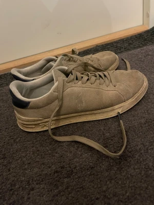 Mockasneakers Polo Ralph Lauren - Snygga beige sneakers i mocka från Polo Ralph Lauren med klassisk låg profil och diskret logga på sidan. Skorna har matchande beige snörning och svart detalj vid hälen. Perfekta för en stilren och avslappnad look.