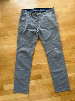 Grå chinos från BOSS - Snygga grå chinos från BOSS med klassisk rak passform. Byxorna har två sidfickor fram och två bakfickor. Tillverkade i ett mjukt bomullstyg som är bekvämt hela dagen. Perfekta för en stilren och avslappnad look.