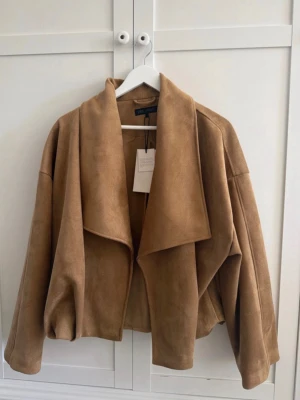 Oversized kappa i mockaimitation Zara - Snygg oversized kappa från Zara i mjuk mockaimitation. Kappan är ljusbrun, har bred krage och avslappnad passform med droppade axlar. Perfekt för dig som gillar trendiga och bekväma ytterplagg med modern look. Helt ny med prislapp kvar 