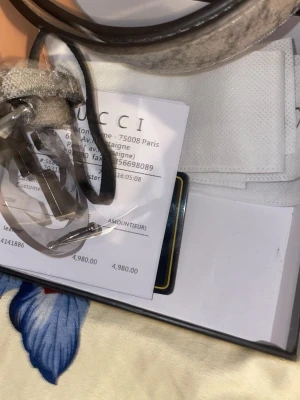 Gucci GG Supreme bälte med silverdetalj - Snyggt Gucci GG Supreme bälte i beige och brunt med klassiskt monogrammönster och stor silverfärgad GG-logga som spänne. Bältet är gjort i skinn och har exklusiv känsla, perfekt för att lyfta vilken outfit som helst.